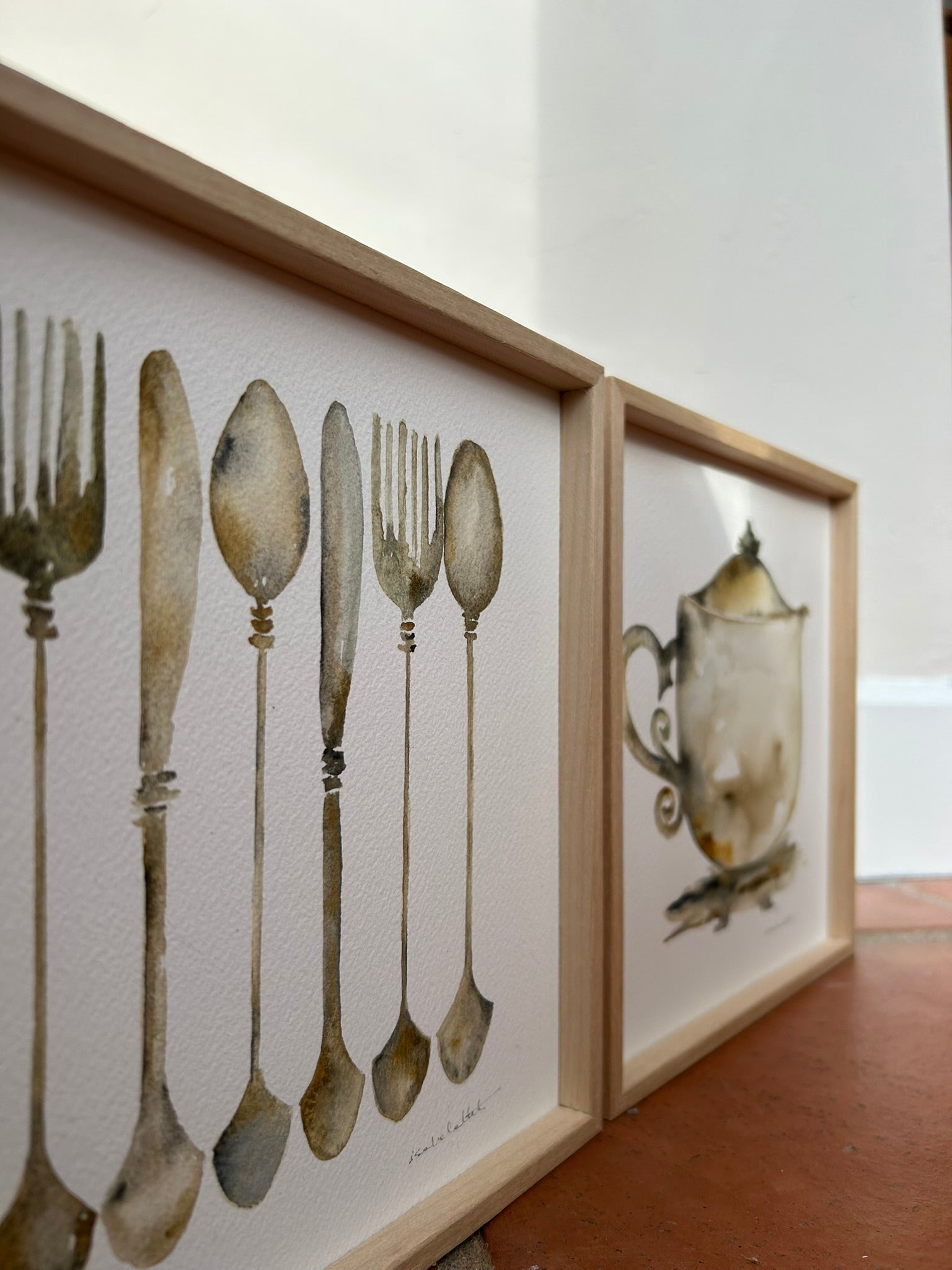 Pareja de cuadros decorativos para la cocina, hay un cuadro con una tetera y otro con unos cubiertos que incluyen una cuchara, un tenedor y un cuchillo, en tonos plata y óxido, imitan una vajilla antigua